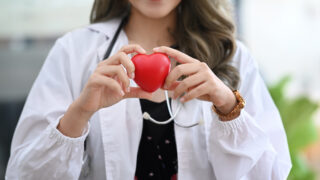Smiling female doctor with stethoscope holding red heart. Cardio