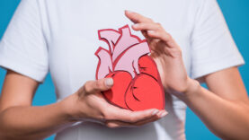 cropped shot of woman in white tshirt holding paper made heart on blue backdrop