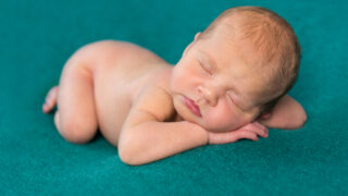 sweet newborn sleeping on stomach and hands with headband