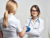 The nurse shakes hands with the patient on a light background and blue gloves with a stethoscope