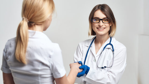 The nurse shakes hands with the patient on a light background and blue gloves with a stethoscope