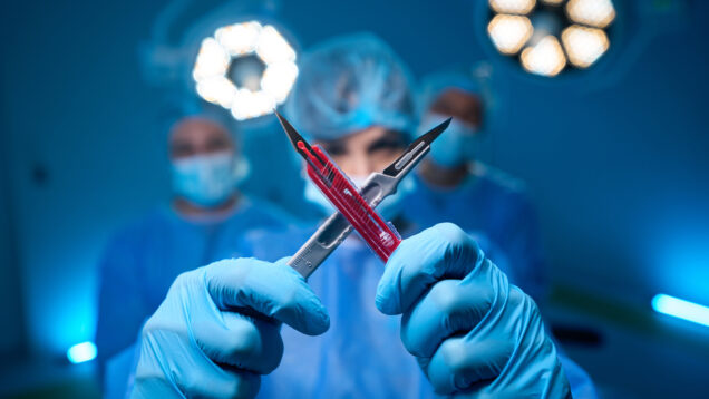 Woman doctor wearing uniform and gloves making x sign with scalpels in surgery