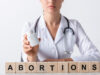 cropped view of doctor holding bottle near cubes with abortion letters