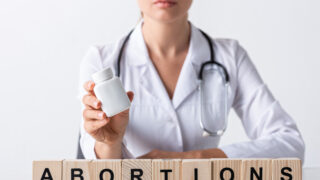 cropped view of doctor holding bottle near cubes with abortion letters