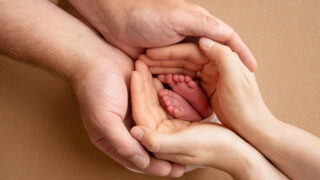 The palms of the parents. A father and mother hold the feet of a newborn child