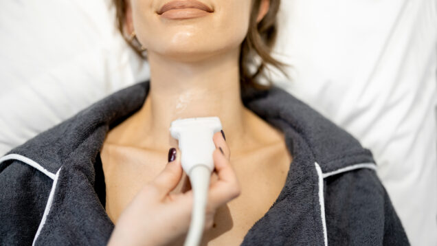 Doctor examining thyroid of female patient with ultrasound scan in clinic